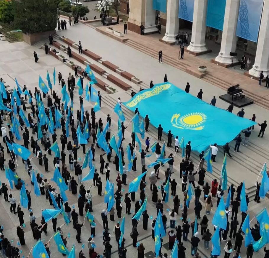 Молодёжь с большим государственным флагом у здания КБТУ в Алматы